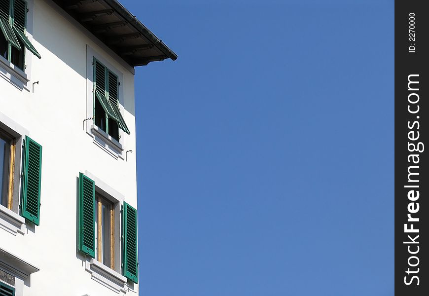 White building with green shutters and wooden frame against blue sky. White building with green shutters and wooden frame against blue sky