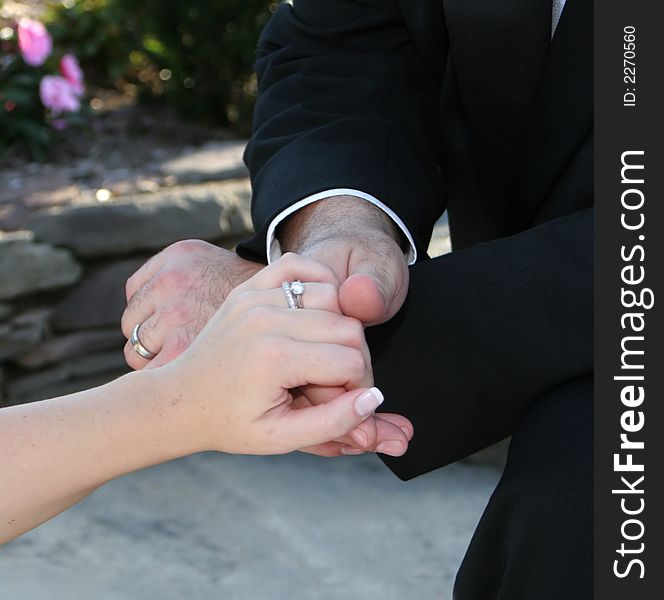 Detail of groom holding bride's hand showing wedding rings in formal attire. Detail of groom holding bride's hand showing wedding rings in formal attire