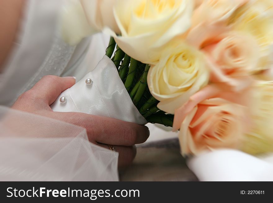 Detail of bride's hand holding bouquet of roses with satin and pearl wrap blur applied to edges for effect. Detail of bride's hand holding bouquet of roses with satin and pearl wrap blur applied to edges for effect