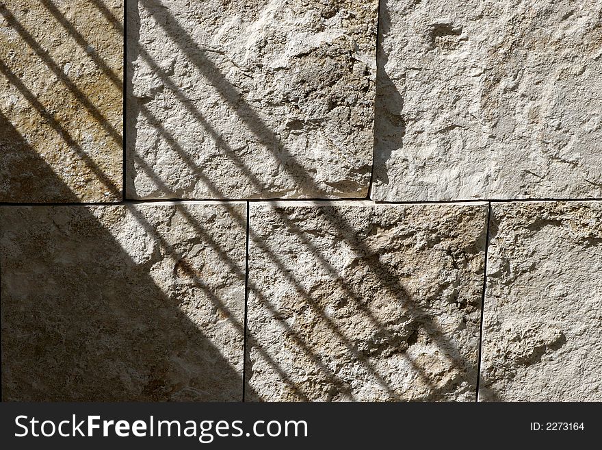 A railing shadow falls diagonally on a textured granite block wall in the afternoon sun. A railing shadow falls diagonally on a textured granite block wall in the afternoon sun.