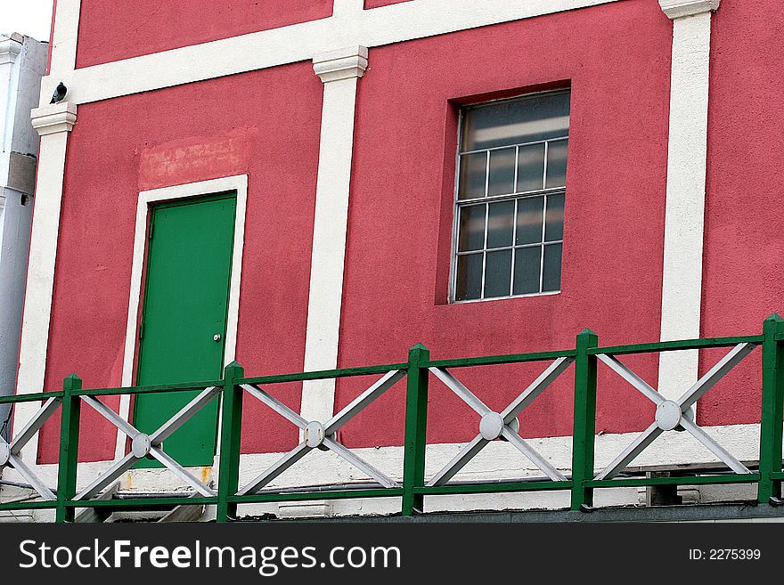 A bright pink stucco apartment or condo with a green door. A bright pink stucco apartment or condo with a green door