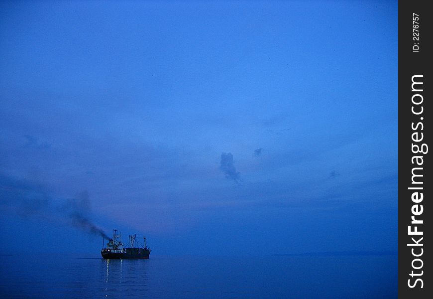 Freighter cargo ship sailing away from pier on a blue twilight. Freighter cargo ship sailing away from pier on a blue twilight