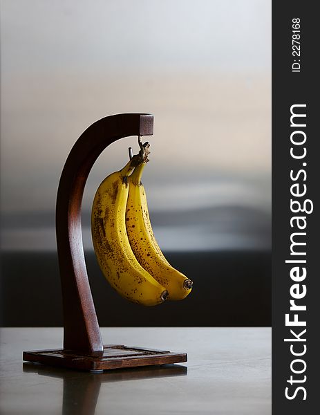 2 ripe bananas on a banana hook hanger in kitchen on counter.  Refrigerator in background. 2 ripe bananas on a banana hook hanger in kitchen on counter.  Refrigerator in background.