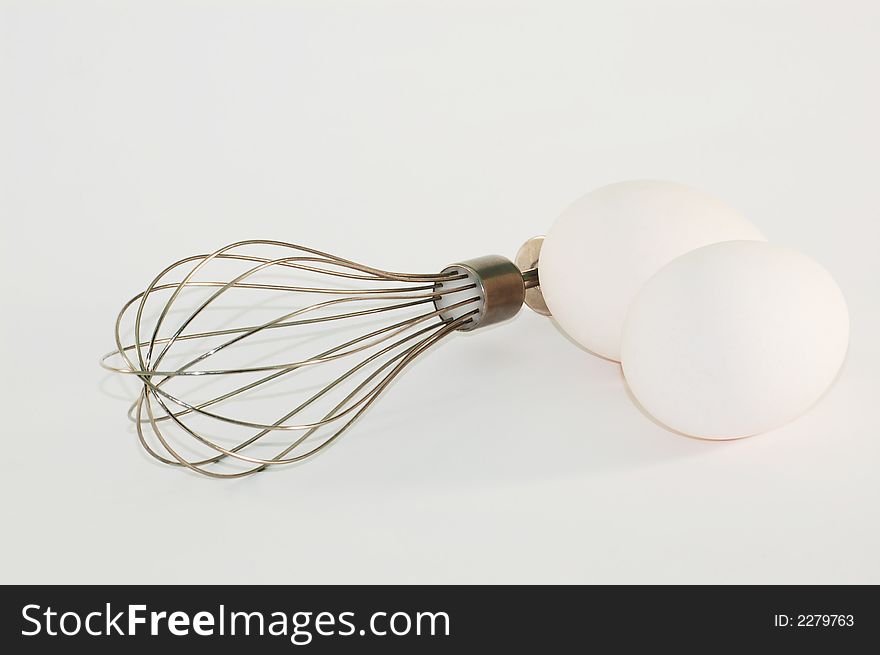 Two eggs and metal whisk on white. Two eggs and metal whisk on white