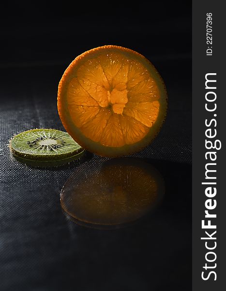 A slice of orange and kiwi slice on a dark background. A slice of orange and kiwi slice on a dark background