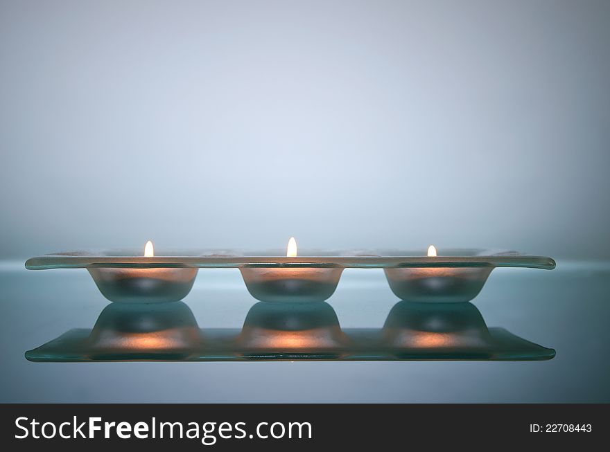 Three candles light in glass holder, on glass table
