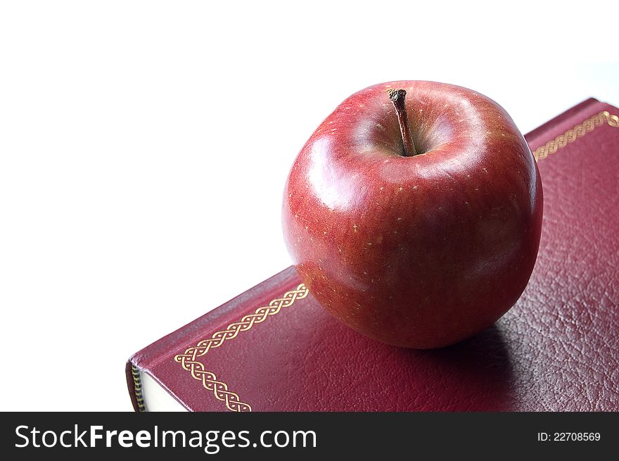 A shiny red apple on a red hardback book for the teacher. Sharp focus on the apple. Copy space. A shiny red apple on a red hardback book for the teacher. Sharp focus on the apple. Copy space.