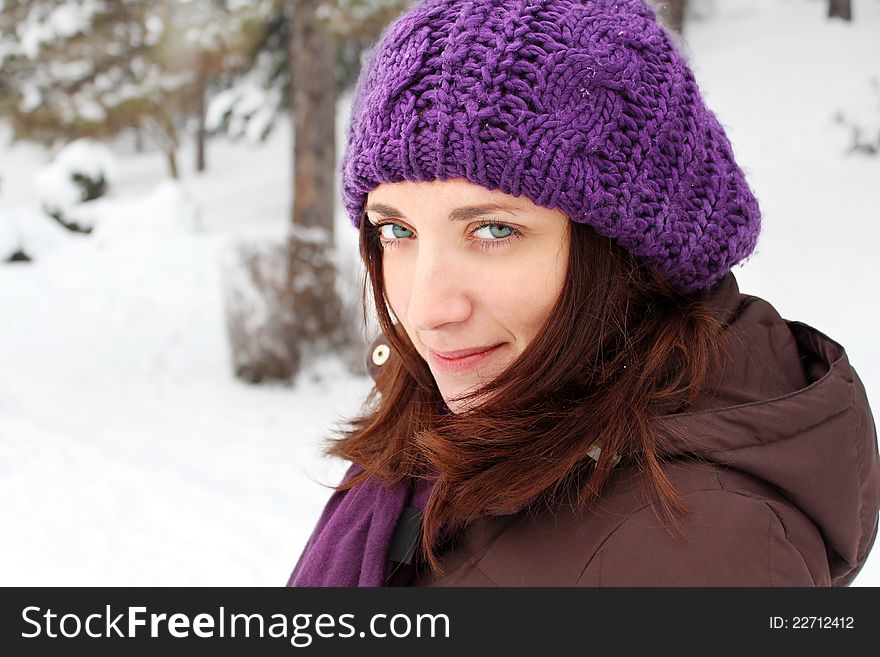 Girl wearing purple hat, smiling, in a park covered with snow