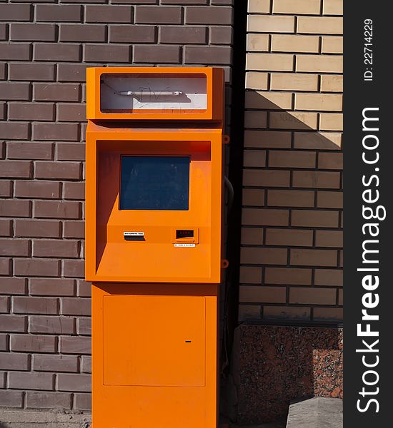 Faulty payment terminal standing on street beside brick wall