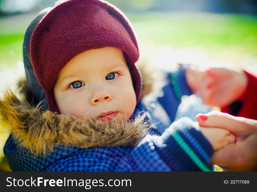 Close-up portrait of a little serious boy in a cap holding his mothers arms. Close-up portrait of a little serious boy in a cap holding his mothers arms