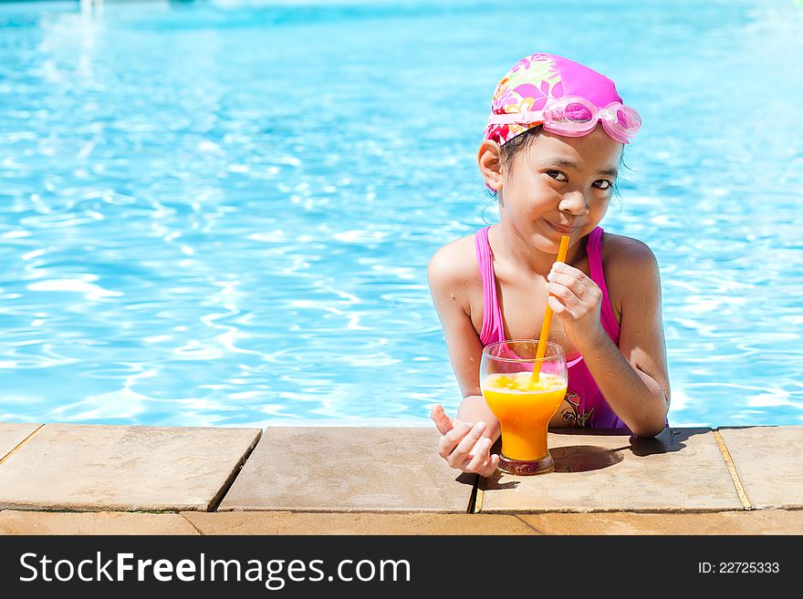 Little girl at swimming pool with orange juice