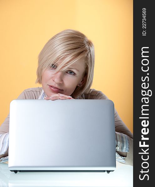 Young woman with a silver laptop on a yellow background looking in camera. Young woman with a silver laptop on a yellow background looking in camera