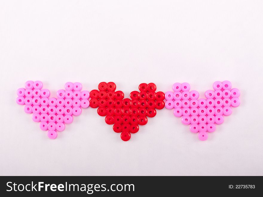 Three plastic love hearts in pink and red made from plastic beads. Three plastic love hearts in pink and red made from plastic beads.