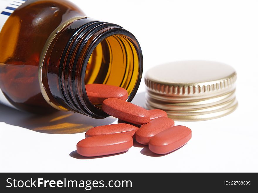 Open pill bottle with medicine spilling out of it with white background