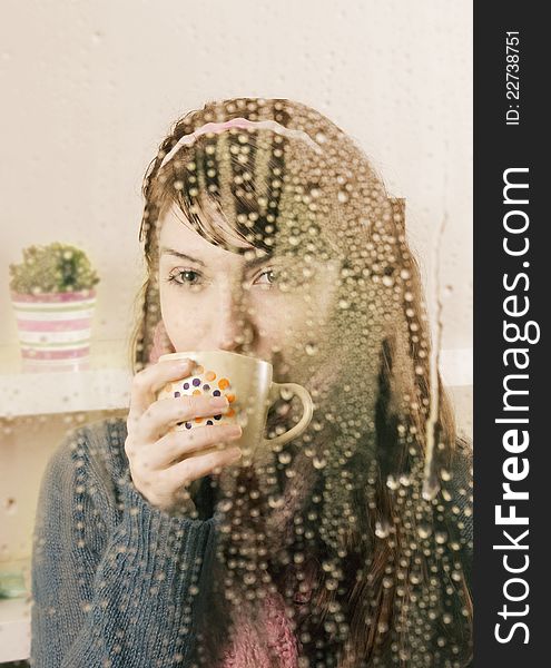 Young woman behind the glass drinking a tea. Young woman behind the glass drinking a tea