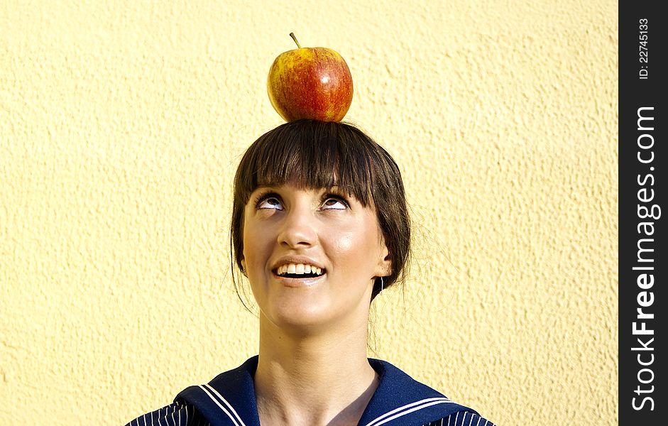 Beautiful happy girl on the background of the wall holds the apple on your head. Beautiful happy girl on the background of the wall holds the apple on your head