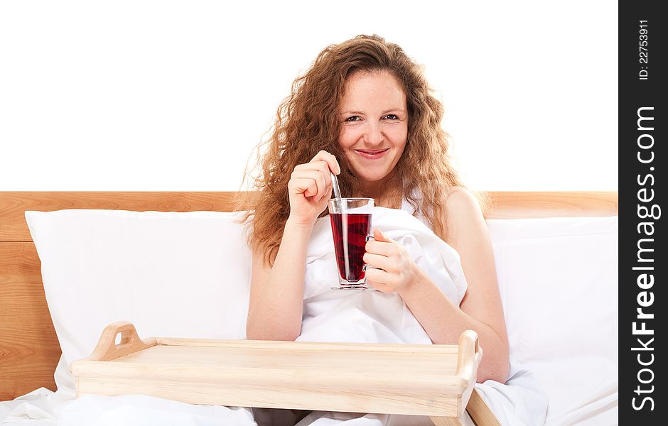 Happy redhead woman in bed with glass of karkade tea  on white