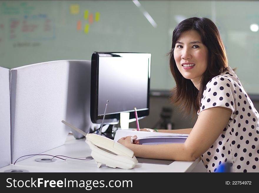 Asian girl at busy office smiling in front of computer. Asian girl at busy office smiling in front of computer.