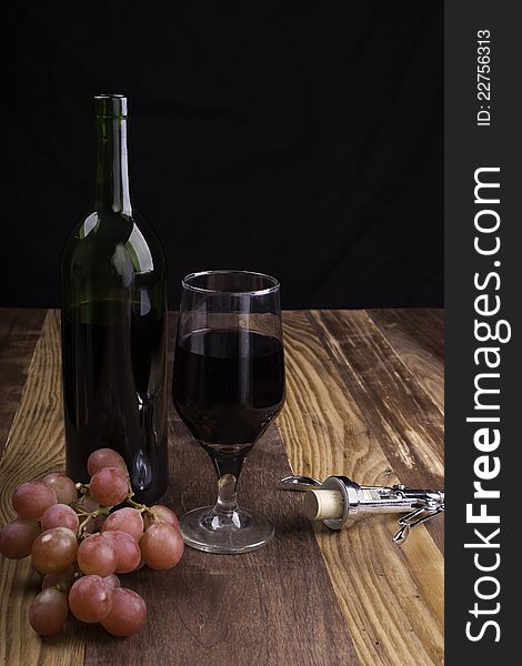 Red wine, red grapes, and corkscrew on wooden table with black background. Red wine, red grapes, and corkscrew on wooden table with black background