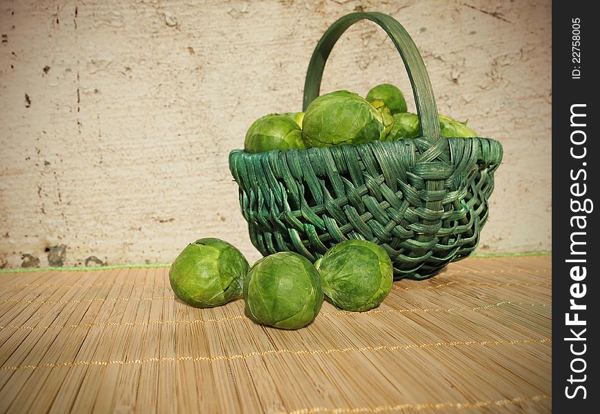 A green basket of fresh green brussels sprouts outside in the sun, against an old stone wall.