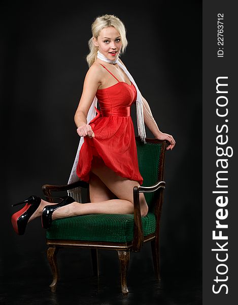 Portrait of lovely tender blonde in red dress, white scarf and high heeled shoes posing on chair in the studio. Portrait of lovely tender blonde in red dress, white scarf and high heeled shoes posing on chair in the studio