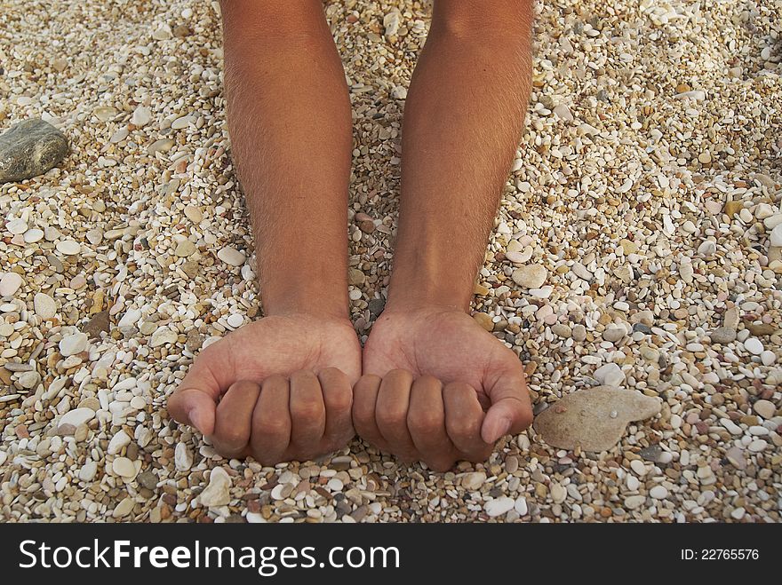Man tanned hands compressed into cams against background of small stones on the beach. Man tanned hands compressed into cams against background of small stones on the beach