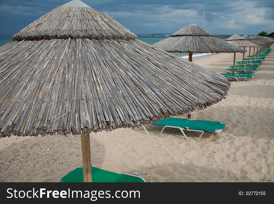 Empty beautiful beach with straw umbrellas and beach beds before the storm. Empty beautiful beach with straw umbrellas and beach beds before the storm