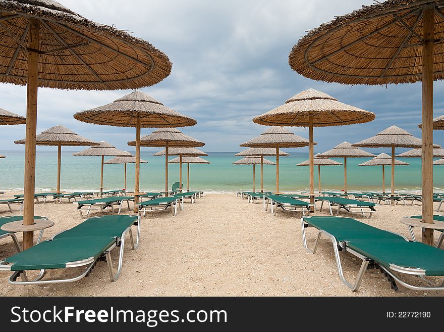 Empty beautiful beach with straw umbrellas and beach beds before the storm. Empty beautiful beach with straw umbrellas and beach beds before the storm