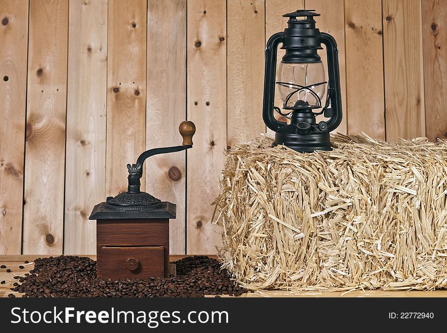 Coffee grinder and beans on wood background with lantern and straw bale