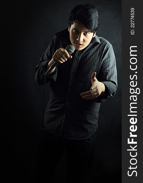 Young man singer with microphone gesture on black background