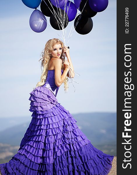 Beautiful girl in the purple dress with balloons in the background sky