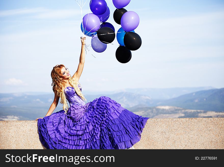 Beautiful girl in the purple dress with balloons in the background sky