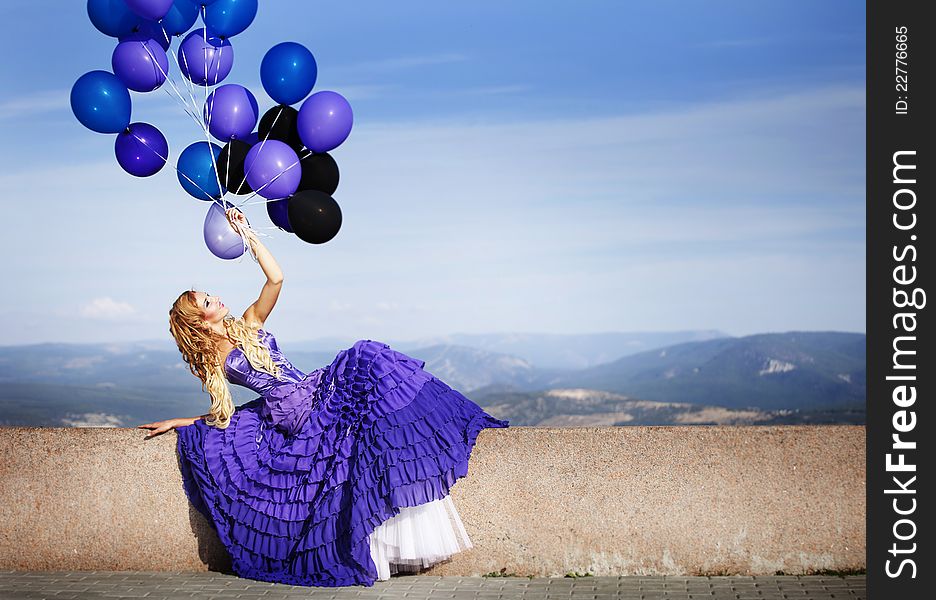 Beautiful girl in the purple dress with balloons in the background sky