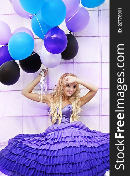 Beautiful girl in the purple dress with balloons in the background sky