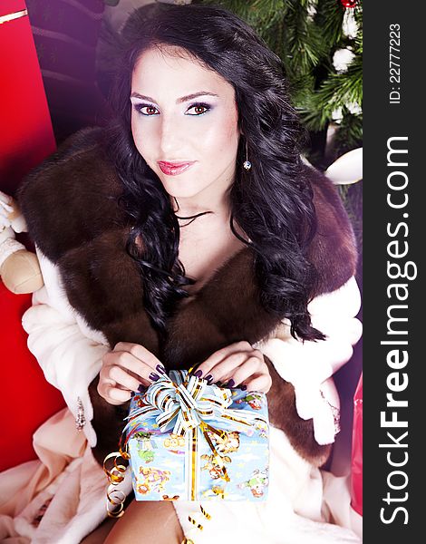 Christmas woman near a Christmas tree holding big gift box while sitting near Christmas Tree. Christmas woman near a Christmas tree holding big gift box while sitting near Christmas Tree