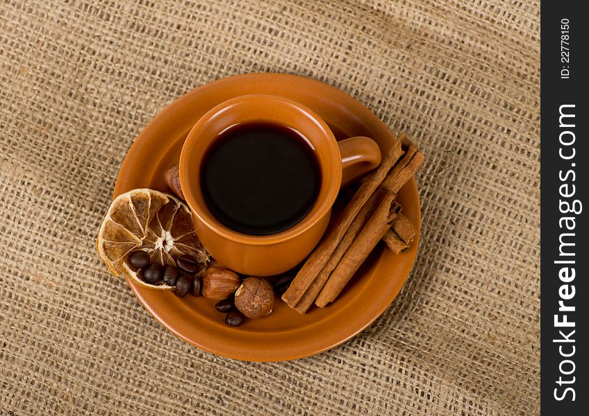 Closeup shot of freshly prepared cup of italian espresso with cinnamon, coffe beans, nuts and lemon over sacking. Closeup shot of freshly prepared cup of italian espresso with cinnamon, coffe beans, nuts and lemon over sacking