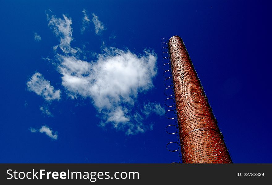 An old factory chimney, white clouds, blue sky.