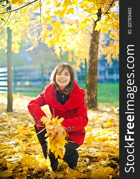 Young laughing woman in red coat is going to throw yellow leaves. Young laughing woman in red coat is going to throw yellow leaves