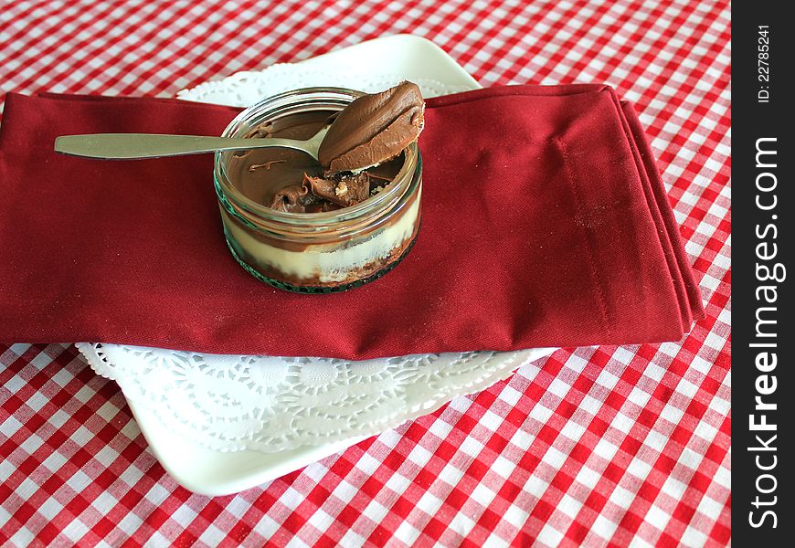 This photo shows a delicious looking single Banoffee Cheesecake in a glass pot sitting on a Red Linen Napkin