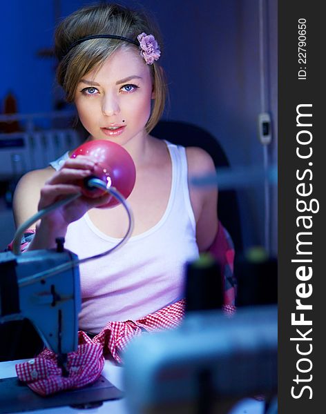 Seductive blond sewing in her workshop a red squared shirt