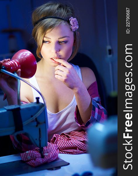 Seductive blond sewing in her workshop a red squared shirt