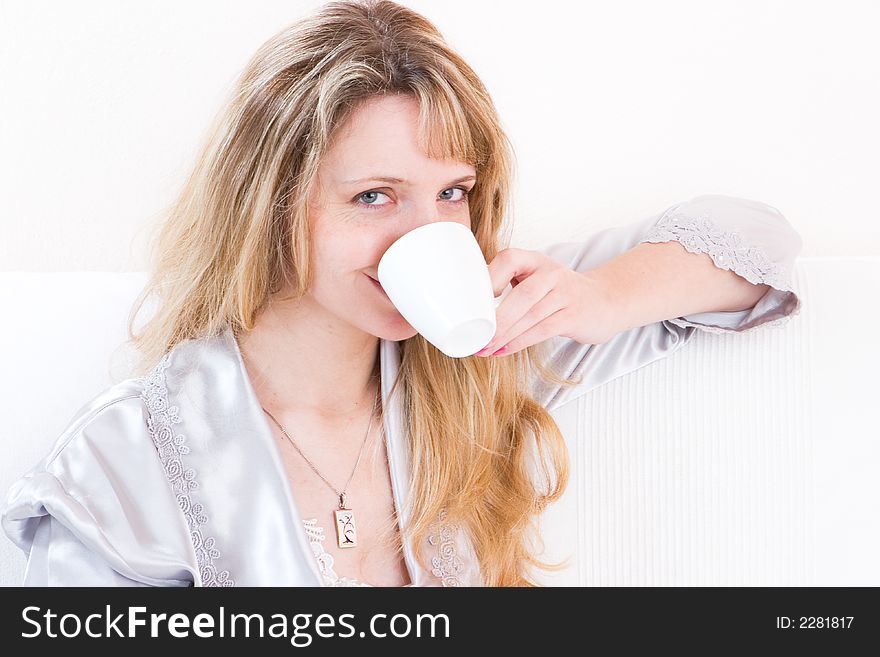 A women in a silver robe smiling whilst drinking a coffee