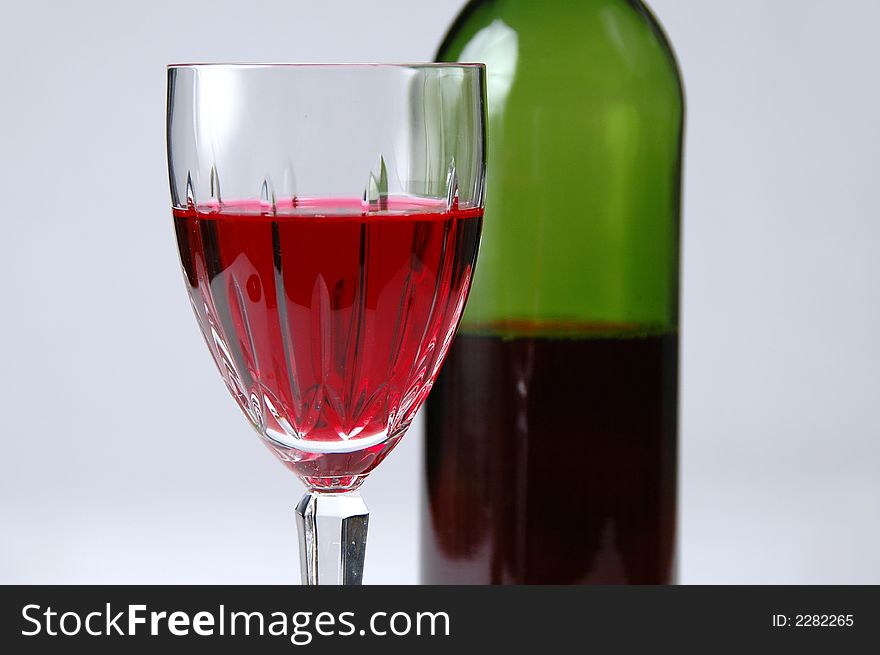 Close-up of glass and bottle of red wine over a neutral background. Close-up of glass and bottle of red wine over a neutral background.