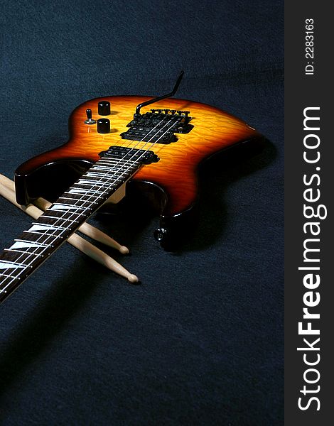 Close up view of electric guitar and drumstick on a black background