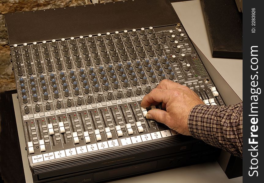 Hand of audio engineer adjusting level controls on an audio mixing board