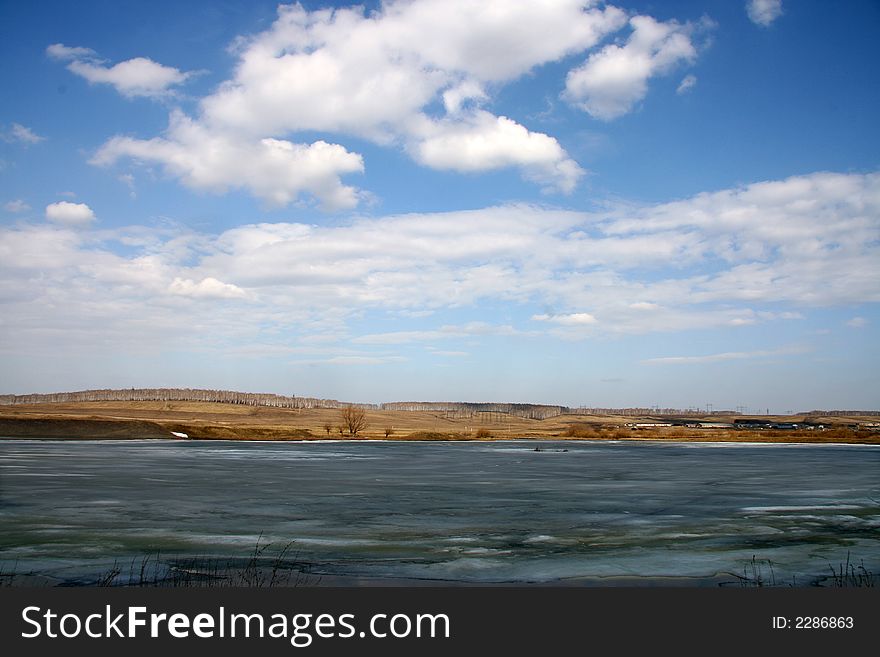 Spring landscape with lake the covered thawing ice and village on a background. Spring landscape with lake the covered thawing ice and village on a background.