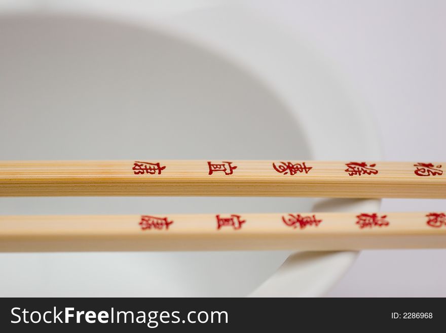 A pair of Chopsticks with red letters on a white bowl