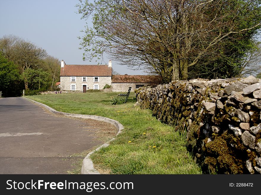 Rural English Road with a dry stone wall in the foreground and farmhouse to the rear
