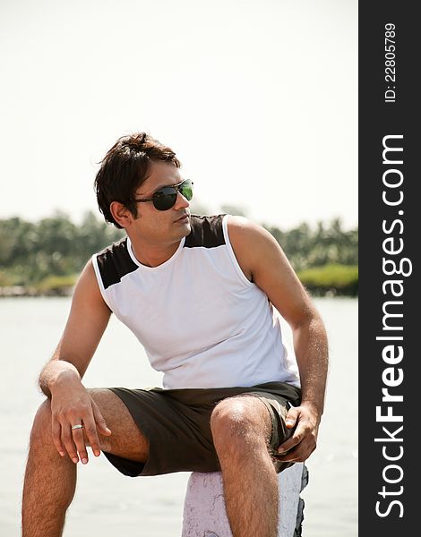 Indian Happy young man sitting on stone out of the water with sunglasses. Indian Happy young man sitting on stone out of the water with sunglasses