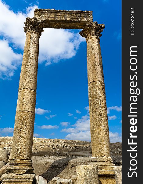 Two ancient Roman columns with capstones support a large flat stone referred to as an abacus. This trio is against a blue sky with a few clouds. Two ancient Roman columns with capstones support a large flat stone referred to as an abacus. This trio is against a blue sky with a few clouds.